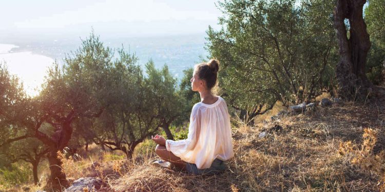 woman in olive field meditating on island in greece at sunset