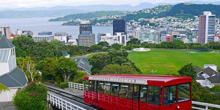 A bright red Wellington cable car moves down its track with the city in the background