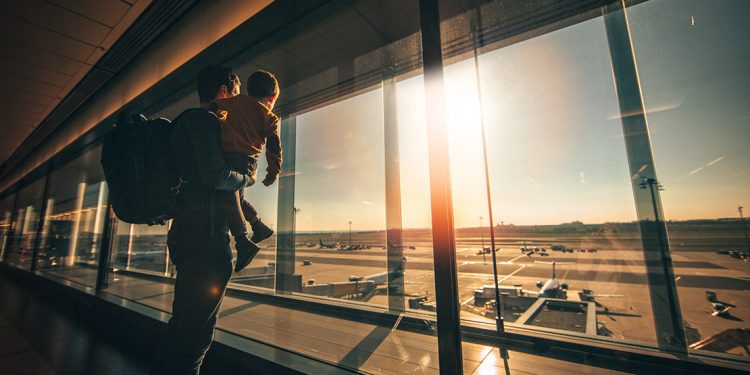 Father and child standing in airport looking out window at planes.