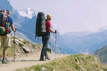 Two backpackers with hiking poles on trail with mountains in background.