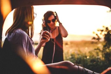 A pair of women on a road trip enjoy an apple and music