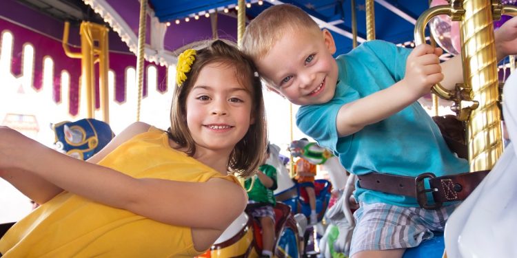 Two cute kids having fun while riding a carousel at an amusement park or carnival