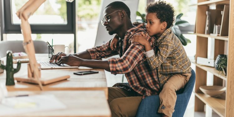 Side view of african-american father and son using laptop while sitting together in office