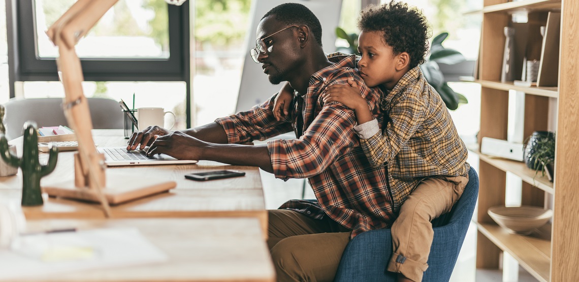 Side view of african-american father and son using laptop while sitting together in office
