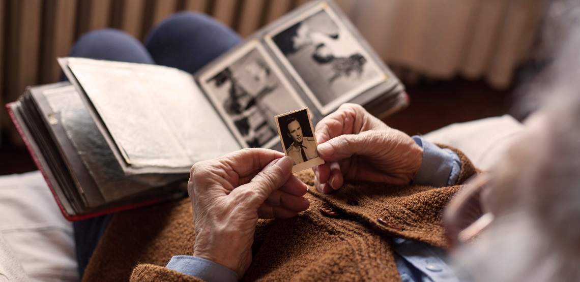 Over-the-shoulder view of a senior adult woman looking at an old photo of her husband