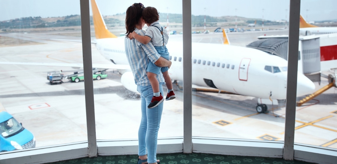 mom holding older baby looking out the window of an airport