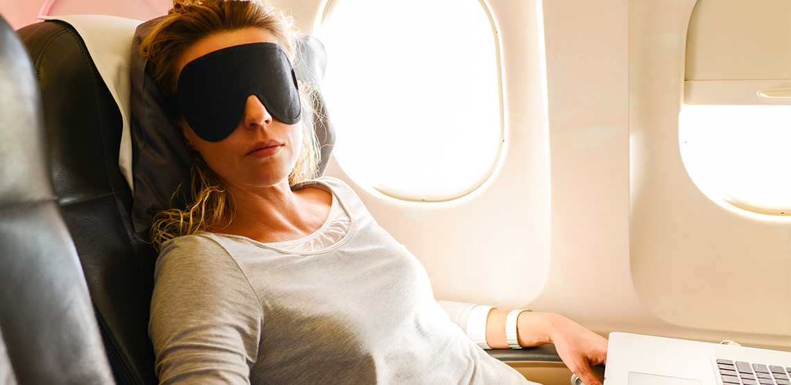 Woman with a sleeping mask and a laptop in front of her on a plane
