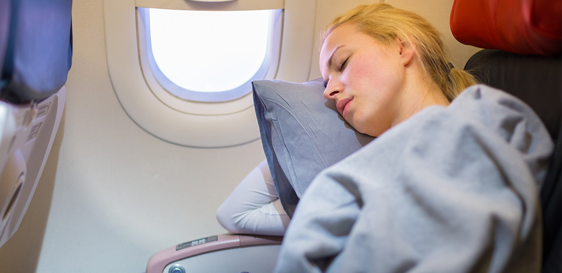 Woman sleeping on a plane with a pillow and blanket