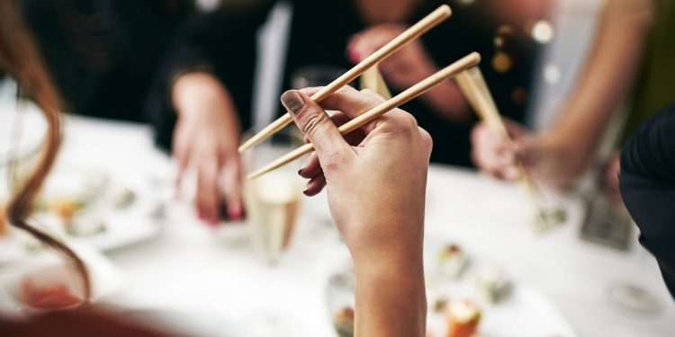 Cropped shot of an unrecognizable person eating with chopsticks during a dinner party