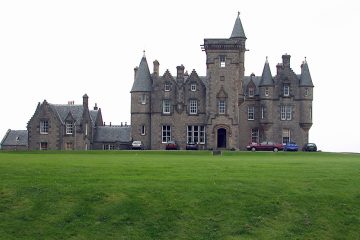 Castle on a hill with cars parked out front.