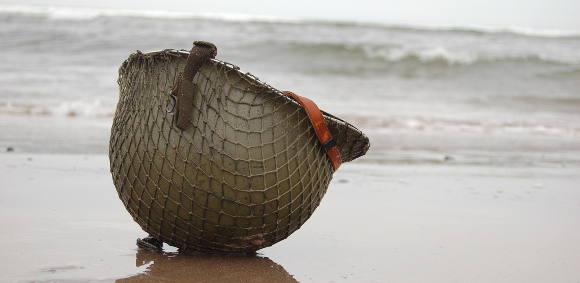 A brown helmet rests on the wet sand while waves lap behind it.
