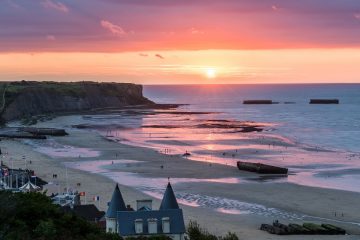 The sun sets purple and orange over a temporary, World War II-era harbor located in Arromanches-les-Bains, France.