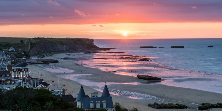 The sun sets purple and orange over a temporary, World War II-era harbor located in Arromanches-les-Bains, France.