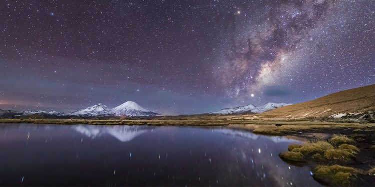 Starry sky over lake and snow-capped mountains