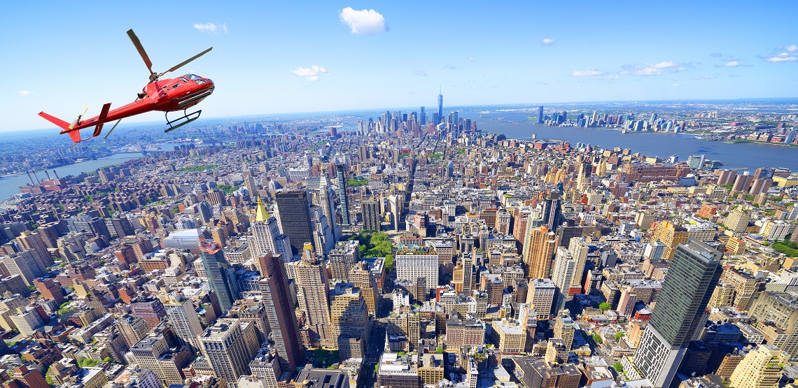 A red helicopter banks over New York's Manhattan neighborhood, famous high rises laid out below it.