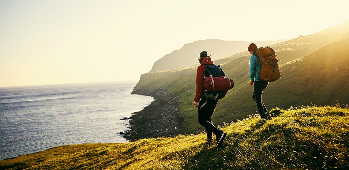 Two people wearing backpacks hiking along the coast