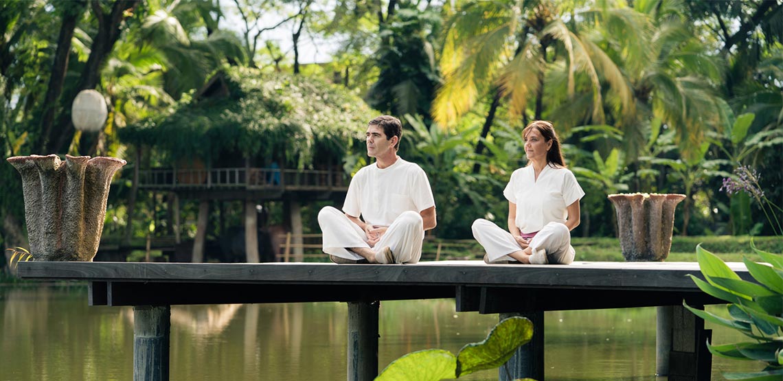 Two people sitting on dock over water with jungle in background