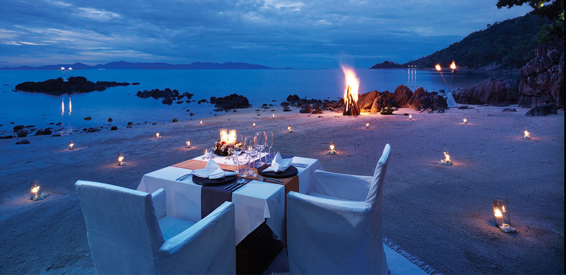 Table with plates on a beach with bonfire