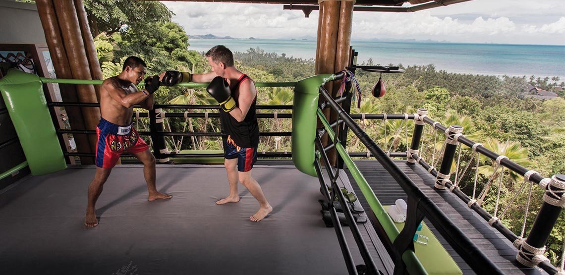 Two men kickboxing on platform overlooking jungle and ocean.