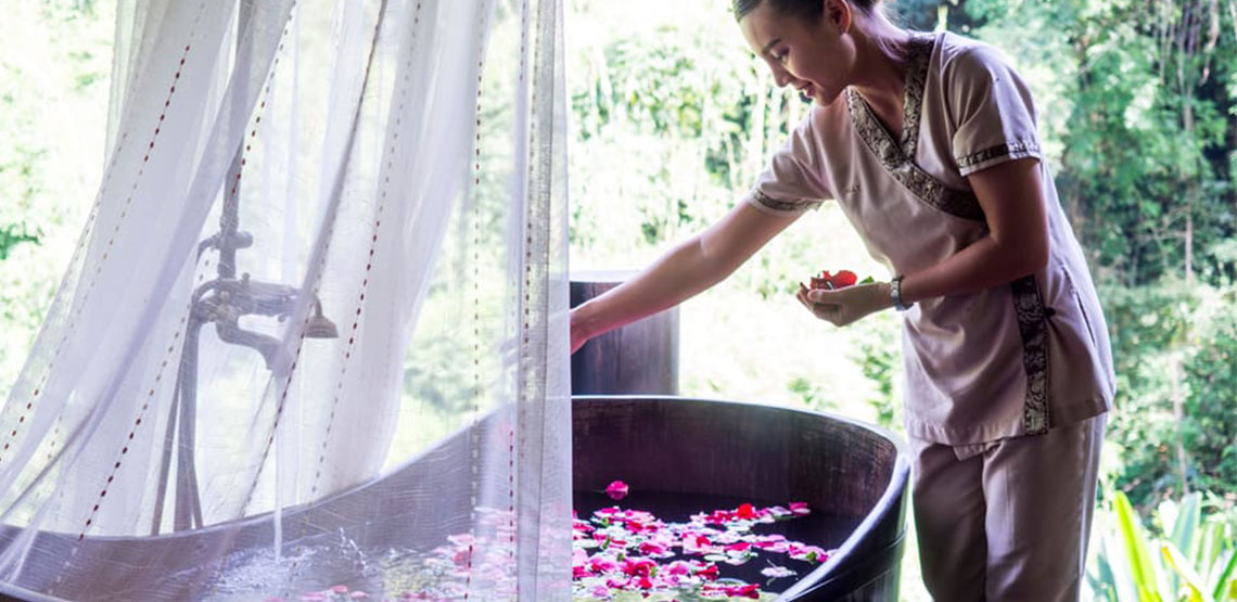 Woman putting flower petals into a bathtub outside