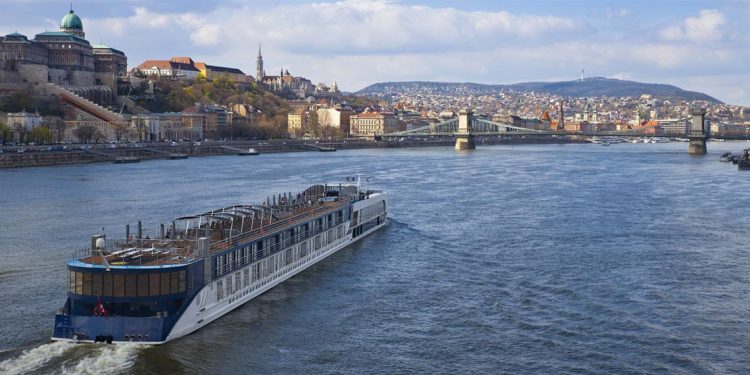 A riverboat cruises on the Danube in Budapest as building-encrusted hills rise before it.