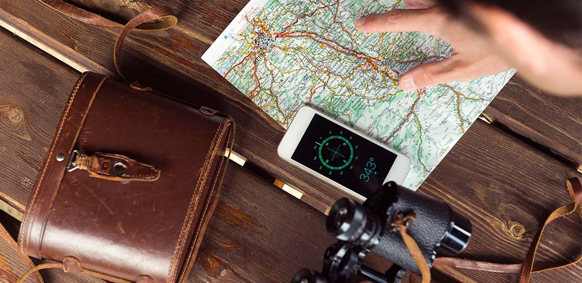 Person pointing at a map with compass open on their phone and binoculars out of case.