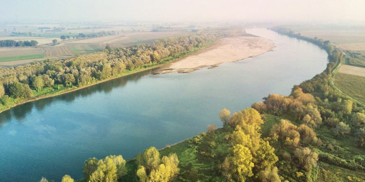 An aerial view of the Po River showing green fields and streets on the banks beside the placid water