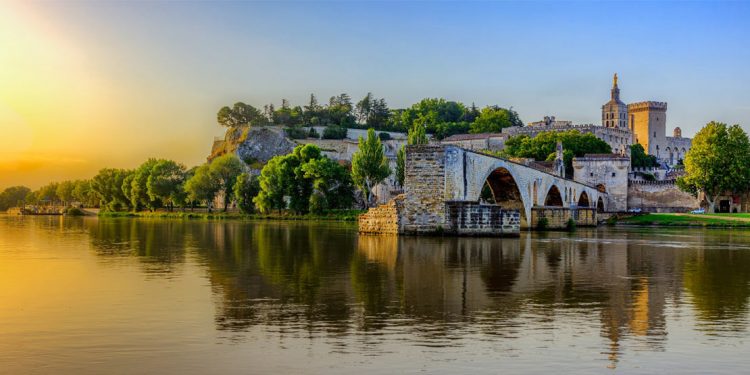 The sunrises over Avignon Bridge and the Pope's Palace in Pont Saint-Benezet, Provence, France, as seen from a river-water view.