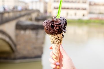 Person holding a cone full of gelato in front of river and bridge in Florence