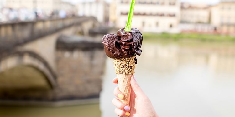 Person holding a cone full of gelato in front of river and bridge in Florence