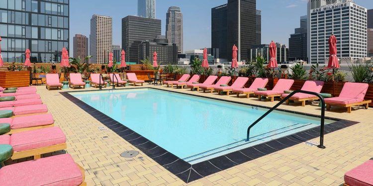 Rooftop pool with pink lounge chairs surrounding and skyscrapers in background