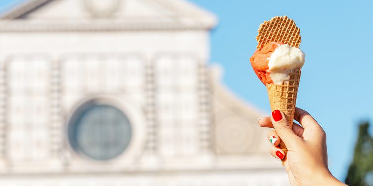 Woman holding cone of gelato up to old building