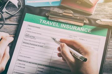 A close up of a travel-insurance application clipped into a clipboard, a pen-holding hand preparing to sign it.