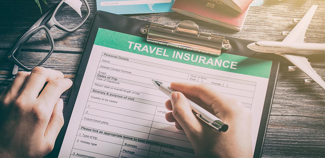 A close up of a travel-insurance application clipped into a clipboard, a pen-holding hand preparing to sign it.