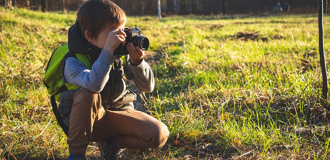 Young boy crouching in a field holding camera to his eye