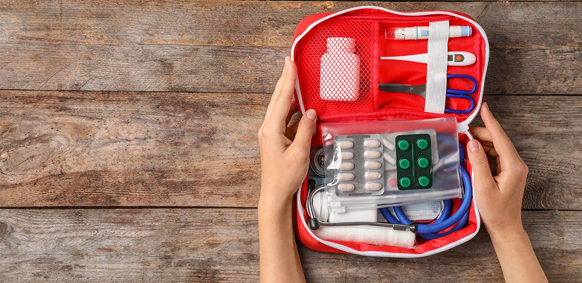 Someone holding an open first aid kit filled with pills, thermometer, stethoscope, scissors, etc.