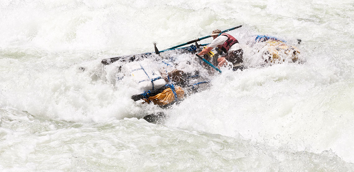 A wave-washed raft crashes through foamy whitewater rapids.