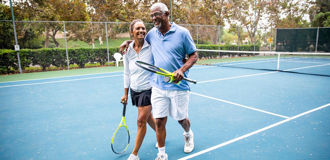 Two people walking off tennis court holding rackets