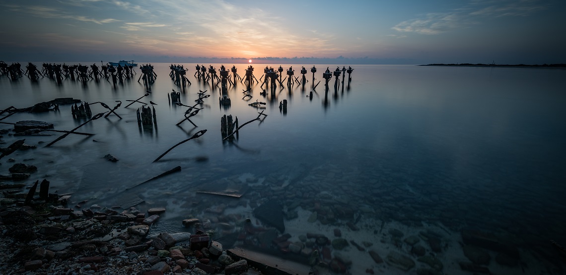 The rising sun at Dry Tortugas National Park turns the water a pearlescent gray and casts the old pylons of a collapsed pier into stark relief.
