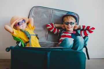 Two kids sitting in a suitcase wearing sunglasses