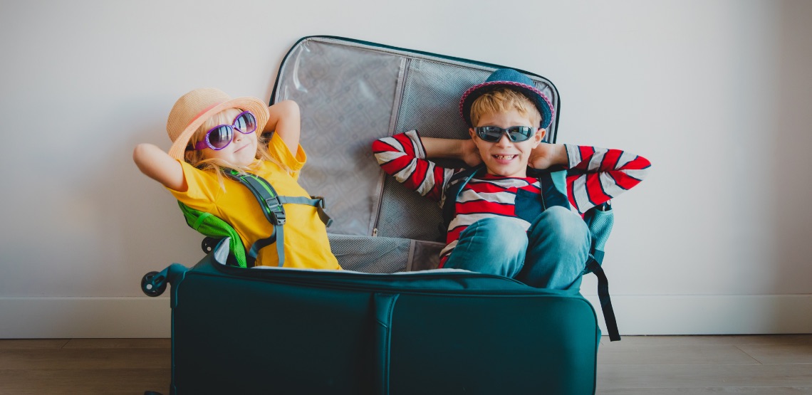 Two kids sitting in a suitcase wearing sunglasses