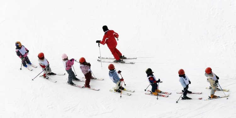 An overhead shot of children lined up in a ski school and their instructor stares off into the distance