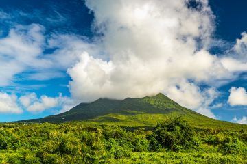 A cloudy cap rests on a green tropical mountain peak.