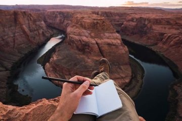 A person with an open notebook in a rocky landscape.