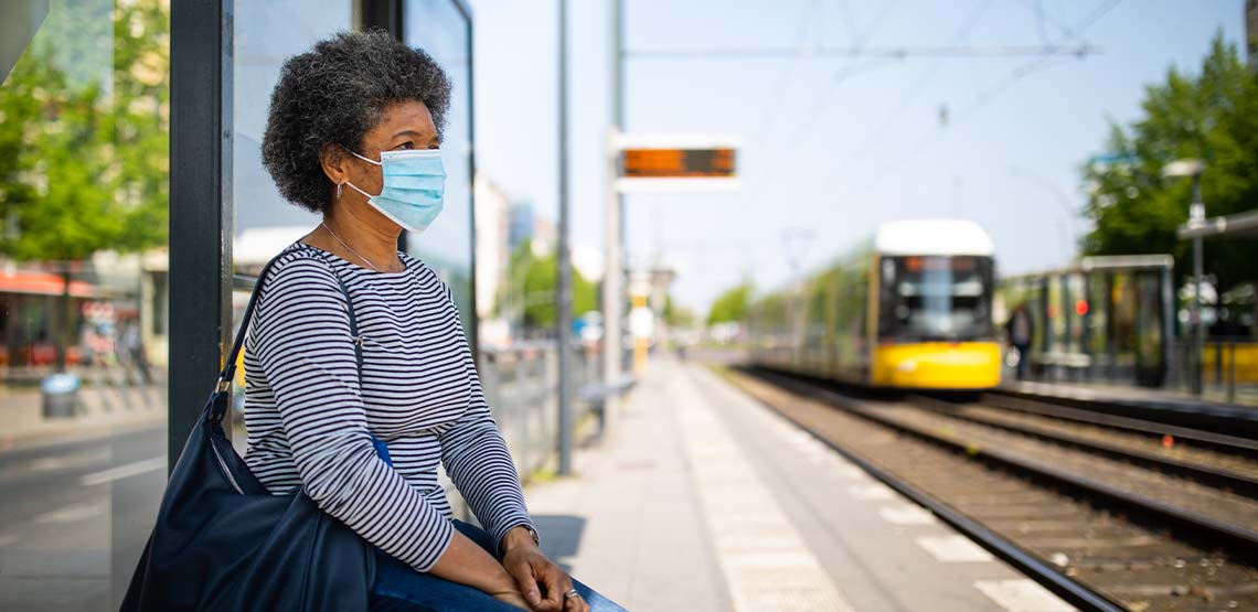Someone wearing a mask while sitting waiting for a train.