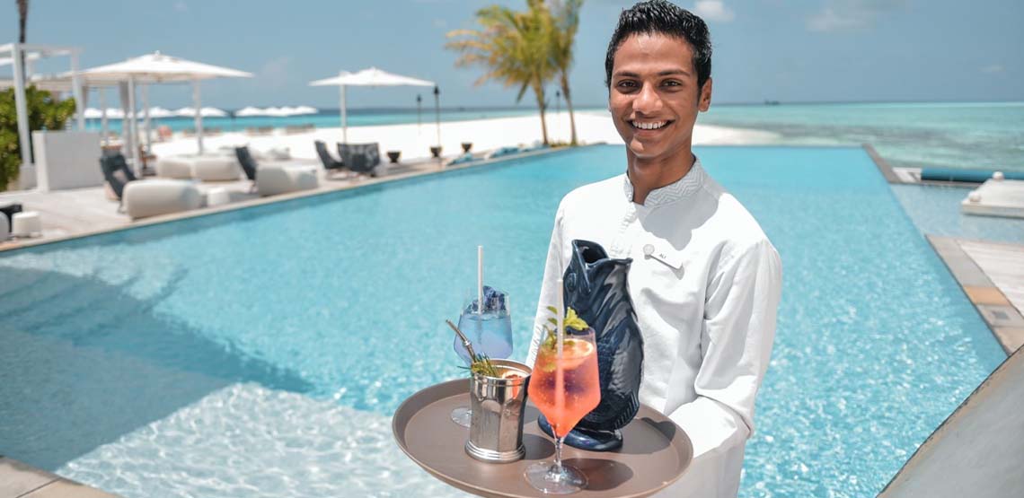 A man holding a tray of drinks in front of a pool.