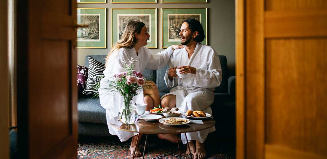 A couple sitting in a hotel room in bathrobes.