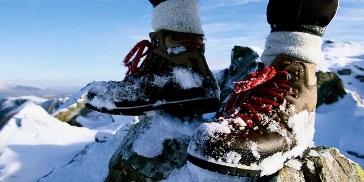A person standing on a snowy mountain wearing brown hiking boots.