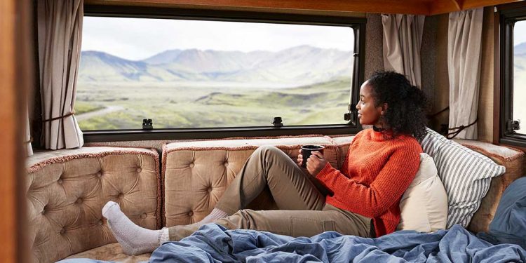 A woman sitting on a couch in an RV with a mug in her hand looking out the window.