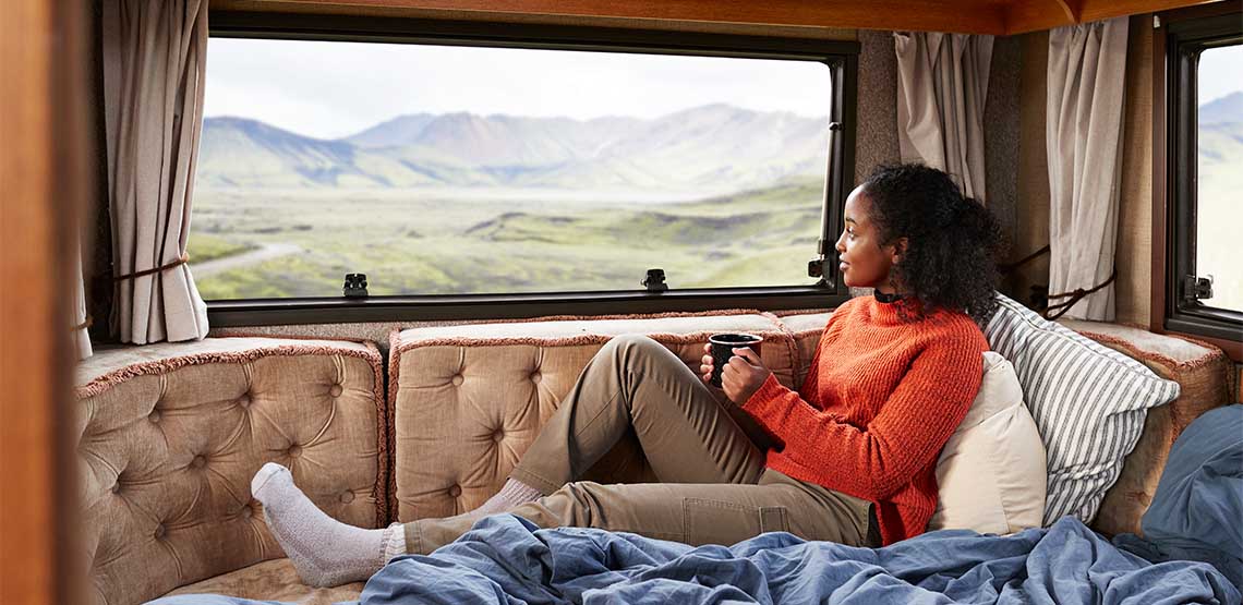 A woman sitting on a couch in an RV with a mug in her hand looking out the window.